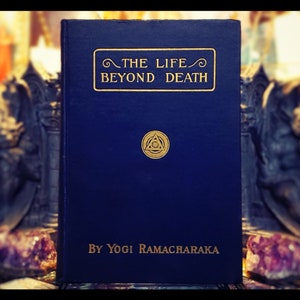 Puede incluir: Un libro de tapa dura azul titulado "The Life Beyond Death" de Yogi Ramacharaka. La portada del libro presenta un símbolo dorado de un triángulo con un círculo en su interior.