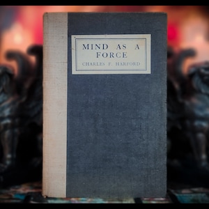 Può includere: Un libro d'epoca intitolato "MIND AS A FORCE" di Charles F. Harford. Il libro ha una copertina blu scuro e un dorso beige chiaro. Il titolo è visualizzato su un'etichetta rettangolare. Un oggetto vintage.