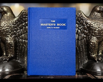 May include: A blue book titled "The Master's Book" by Carl H. Claudy, flanked by two bronze eagle bookends. The book has a textured cover with gold lettering. The eagle bookends are detailed with outstretched wings.