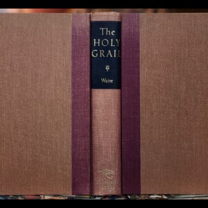 May include: A closed book with a brown linen cover and a burgundy spine. The title on the spine reads "The Holy Grail" by "Waite".