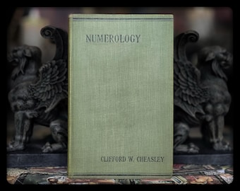 May include: A vintage green book titled "Numerology" by Clifford W. Cheasley. The book has a textured cover and gold lettering.