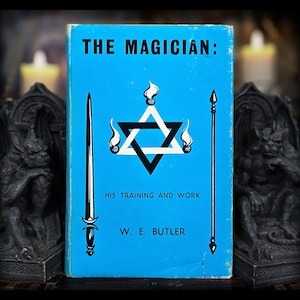 May include: A vintage book titled "THE MAGICIAN: HIS TRAINING AND WORK" by W. E. Butler. The book cover is light blue with a black and white Star of David design, flames, a sword, and a staff. The book is flanked by two dark gargoyle statues.