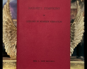 May include: A red hardback book titled "Nature's Symphony or Lessons in Number Vibration" by Mrs J. Dow Balliett.
