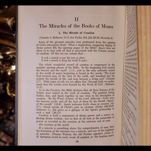 Może przedstawiać: Zbliżenie na stronę książki zatytułowanej "Cuda Ksiąg Mojżeszowych". Strona jest poż&oacute;łkła, a tekst jest brązowy. Tekst omawia stworzenie świata i rolę Tr&oacute;jcy Świętej w stworzeniu.