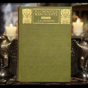 May include: A green hardcover book titled "Illuminated Manuscripts" by J.A. Herbert, with gold lettering and decorative details. The background includes eagle statues and lit candles, creating a vintage aesthetic.