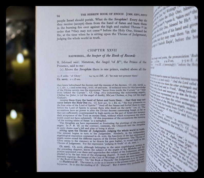 May include: An open book displaying text from "The Hebrew Book of Enoch". The page shows the chapter title "Chapter XXVII" and the name "Radweriel". The book is open on a dark surface, with a blurred background.