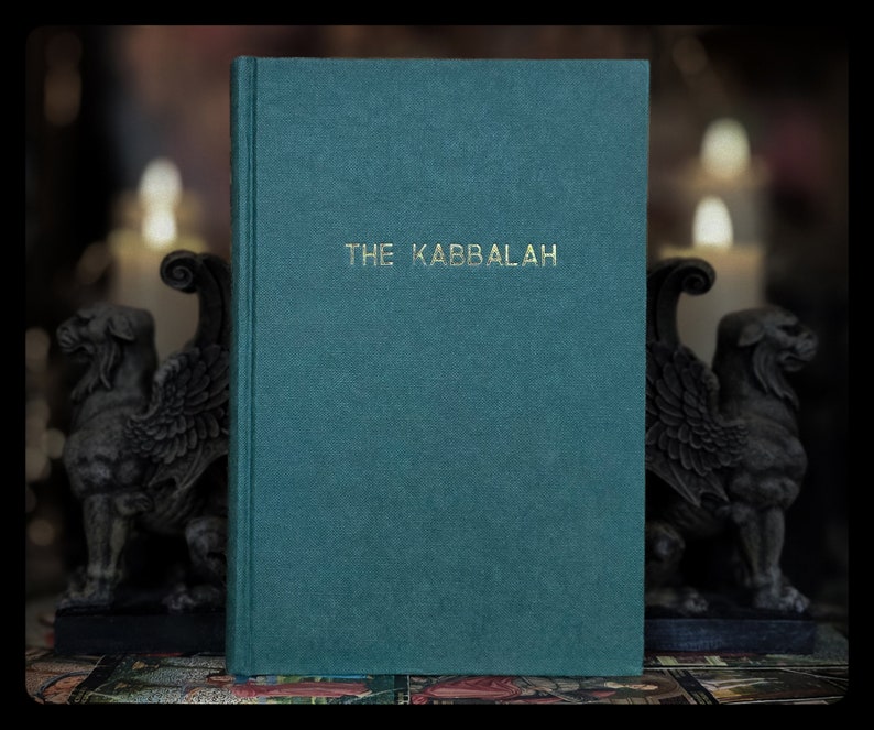 K&ouml;nnte beinhalten: Ein teal-farbenes Buch mit dem goldenen Titel "THE KABBALAH". Das Buch hat einen strukturierten Einband und steht aufrecht. Im Hintergrund befinden sich zwei steinerne Greifenstatuen und verschwommene Kerzen, was eine mystische Atmosph&auml;re erzeugt.