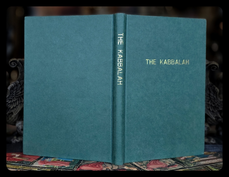 K&ouml;nnte beinhalten: Ein aufgeschlagenes Buch mit t&uuml;rkisfarbenem Einband, betitelt "THE KABBALAH" in goldener Schrift. Der Titel ist auch vertikal auf dem Buchr&uuml;cken aufgedruckt. Der Einband des Buches hat eine strukturierte Oberfl&auml;che. Der Hintergrund ist dunkel.