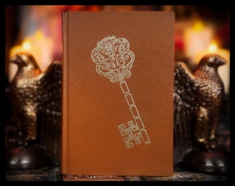 May include: A brown leather-bound book with a gold embossed key design on the front cover. The key has intricate details and a decorative top.