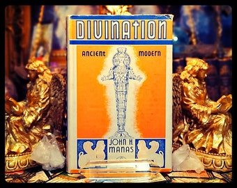 Op de afbeelding: Een vintage boek getiteld "Divination: Ancient & Modern" door John H. Manas. De boekomslag toont een vrouw in een lange, vloeiende jurk die op een trap staat. Het boek is omringd door gouden standbeelden en kristallen.