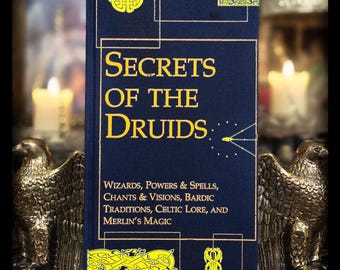 May include: A hardcover book titled "Secrets of the Druids" with gold lettering on a dark blue cover. The book includes text about wizards, spells, chants, and Celtic lore. Two bronze eagle statues flank the book, with lit candles in the background.