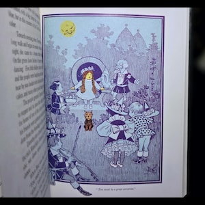 Puede incluir: Ilustraci&oacute;n de un libro en tonos azules y blancos, que representa a un grupo de ni&ntilde;os con trajes fant&aacute;sticos, un perro peque&ntilde;o y una luna sonriente. La obra de arte tiene un estilo detallado y vintage, evocando nostalgia y fantas&iacute;a.