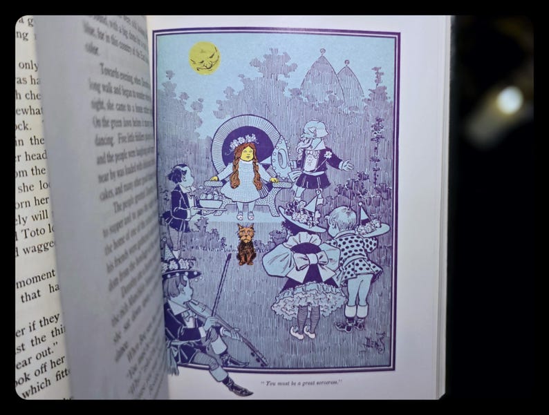 Puede incluir: Ilustraci&oacute;n de un libro en tonos azules y blancos, que representa a un grupo de ni&ntilde;os con trajes fant&aacute;sticos, un perro peque&ntilde;o y una luna sonriente. La obra de arte tiene un estilo detallado y vintage, evocando nostalgia y fantas&iacute;a.