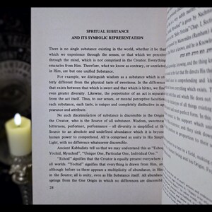 K&ouml;nnte beinhalten: Ein offenes Buch mit dem Titel "SPRITUAL SUBSTANCE AND ITS SYMBOLIC REPRESENTATION" wird von einer brennenden Kerze beleuchtet. Der Text behandelt die Natur der Substanz und ihre symbolische Darstellung, mit sichtbaren Seitenzahlen.