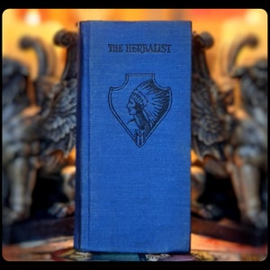 May include: A blue hardcover book titled "The Herbalist" with a Native American profile in a headdress on the front cover.