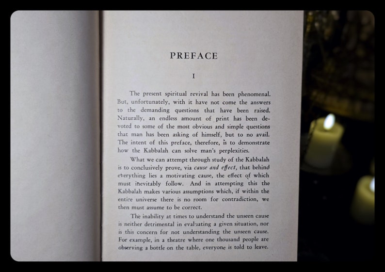 K&ouml;nnte beinhalten: Aufgeschlagenes Buch mit dem Titel "PREFACE" oben. Der Text ist in schwarzer Schrift auf gealtertem, cremefarbenem Papier gedruckt. Das Bild wird von weichem Licht beleuchtet, mit verschwommenen Kerzen im Hintergrund. Der Text behandelt spirituelle Erneuerung und die Kabbalah.