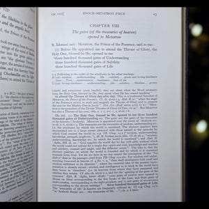 May include: An open book with text, featuring the title "ENOCH-METATRON PIECE" and the chapter heading "CHAPTER VIII". The pages display detailed text, likely from a religious or historical text, with a dark background.