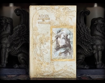 May include: A vintage book with a white cover and gold lettering. The title is "Alice's Adventures in Wonderland". The cover features an illustration of a woman with long dark hair and a white dress.