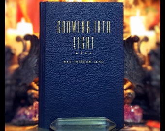Op de afbeelding: Een donkerblauw hardback boek met gouden letters met de titel "Growing into Light" door Max Freedom Long.