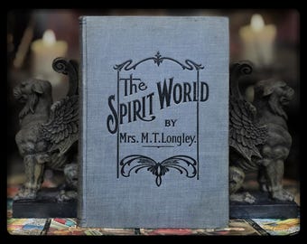 May include: A vintage, blue, hardcover book titled "The Spirit World" by Mrs. M.T. Longley. The book is displayed on a shelf with two decorative gargoyle bookends.