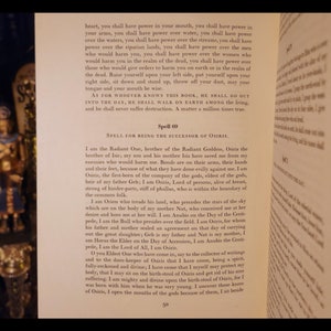 以下が含まれることがあります： 黄ばんだページの開いた本、テキストのクローズアップ、「Spell 00, SPELL FOR BEING THE SUCCESSOR OF OSIRIS.」テキストは、エジプトの神オシリスとそのエジプト神話における役割について説明しています。