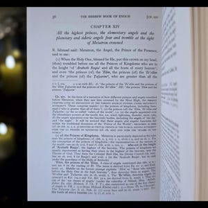 May include: An open book displaying text from The Hebrew Book of Enoch, Chapter XIV. The text describes angels and heavenly beings. The pages are yellowed, and the text is in black. The book is open to a chapter with detailed text.