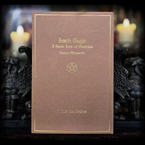 Puede incluir: Un libro marrón titulado "Earth Magic" con letras doradas y un borde dorado. La portada del libro presenta el texto "A Dianic Book of Shadows" y el nombre del autor, Marion Weinstein. También es visible un pentagrama.