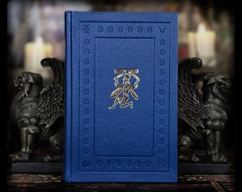 Könnte beinhalten: Ein blaues Hardcover-Buch mit einem silbernen Emblem einer knienden Figur, die einen Stab hält. Das Buch wird von zwei dunkelgrauen Gargoyle-Buchstützen flankiert. Das Buch hat einen dekorativen Rand und einen strukturierten Einband.
