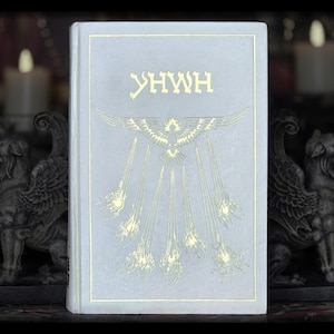 May include: A light blue book with the word "YHWH" printed in gold lettering on the front cover. The book features a stylized image of a bird with wings spread wide, surrounded by rays of light.