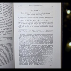 May include: An open book with English text discussing Enoch and Metatron. The right-hand page is fully visible, the left partially. The book has aged pages and a dark background.