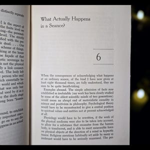 May include: Open book page with text: "What Actually Happens in a Seance?" and the number "6". The text is in black font on a cream-colored page. The book is slightly angled.