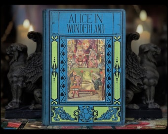 May include: A vintage hardcover book with a blue cover and a green and black border. The title "Alice in Wonderland" is printed in black on the front cover. The cover features an illustration of a scene from the book.