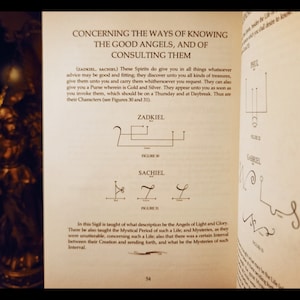 K&ouml;nnte beinhalten: Eine Seite aus einem Buch &uuml;ber Engel, die die Sigillen von Zadkiel und Sachiel zeigt. Der Text beschreibt, wie man diese Engel um Rat und Sch&auml;tze bittet. Die Sigillen sind in schwarzer Tinte auf einer cremefarbenen Seite gezeichnet.