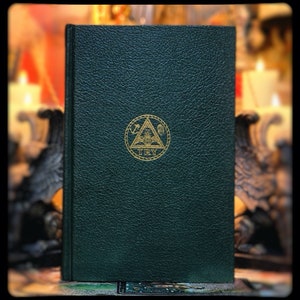 Puede incluir: Un libro encuadernado en cuero verde oscuro con un s&iacute;mbolo dorado en relieve de un tri&aacute;ngulo que contiene una br&uacute;jula y un cuadrado. El s&iacute;mbolo est&aacute; rodeado de un c&iacute;rculo con la palabra "TRY" inscrita debajo.