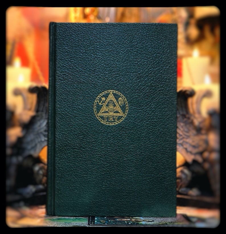 Puede incluir: Un libro encuadernado en cuero verde oscuro con un s&iacute;mbolo dorado en relieve de un tri&aacute;ngulo que contiene una br&uacute;jula y un cuadrado. El s&iacute;mbolo est&aacute; rodeado de un c&iacute;rculo con la palabra "TRY" inscrita debajo.