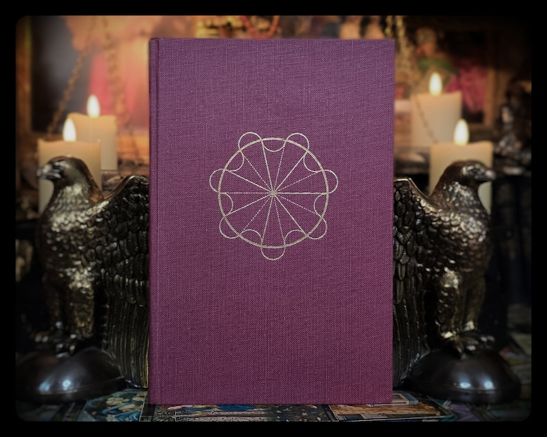 Pode incluir: Um livro de capa dura de cor roxo escuro com um design geom&eacute;trico dourado na capa. O design &eacute; um c&iacute;rculo com oito pontos e uma estrela central.