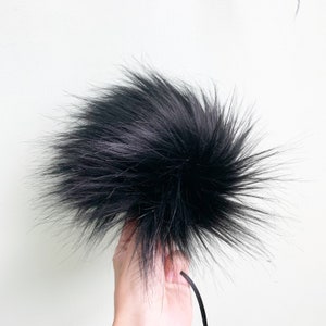 May include: A black fluffy pom pom with a black cord attached.