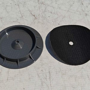 May include: Two-piece set featuring a dark gray, circular base with a central cone and a black, circular pad with a central hole. The items are likely components of a tool or device.