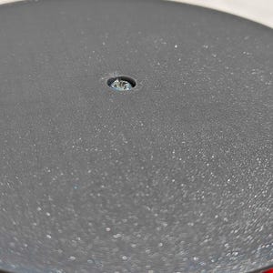 May include: Close-up of a black, circular object with a textured surface. A small screw is visible in the center. The object appears to be part of a larger piece of equipment or furniture.
