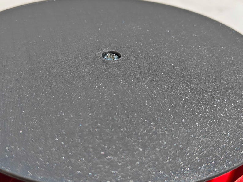 May include: Close-up of a black, circular object with a textured surface. A small screw is visible in the center. The object appears to be part of a larger piece of equipment or furniture.