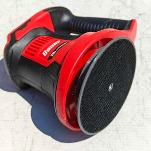 May include: A red and black Bauer 20V Lithium random orbital sander. The sander has a black grip, a red housing, and a round, black sanding pad. The Bauer logo is visible on the side.