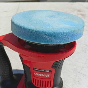 May include: A red and black Bauer 20V Lithium polisher with a light blue foam pad attached. The polisher has a black handle and a red body. The Bauer logo is visible on the side.