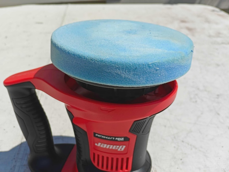 May include: A red and black Bauer 20V Lithium polisher with a light blue foam pad attached. The polisher has a black handle and a red body. The Bauer logo is visible on the side.