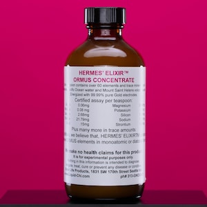 May include: A brown glass bottle with a black cap, labeled "HERMES' ELIXIR ORMUS CONCENTRATE." The label lists ingredients and trace minerals. The bottle is against a magenta background.