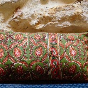 May include: A green and red patterned lumbar pillow with a floral design. The pillow is on a blue and white patterned surface.