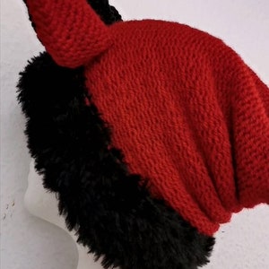 Puede incluir: Un gorro de punto rojo y negro con un ribete negro y peludo. El gorro tiene un dise&ntilde;o puntiagudo en forma de oreja en la parte superior. El gorro se exhibe en una cabeza de maniqu&iacute; blanca. El gorro est&aacute; hecho de un material suave y texturizado.