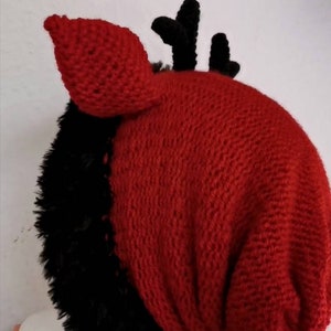 Puede incluir: Un gorro de punto rojo y negro hecho a mano con un dise&ntilde;o &uacute;nico. El gorro presenta una parte superior de punto rojo con piel sint&eacute;tica negra y peque&ntilde;os cuernos negros. El gorro est&aacute; dise&ntilde;ado para ser usado en la cabeza.