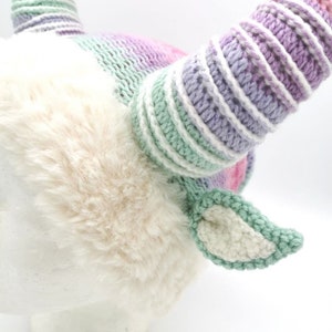 May include: A whimsical, handmade unicorn horn headband. The horns are striped with pastel colors, including pink, purple, and green. The base is covered in soft, cream-colored faux fur, with matching ears. A unique accessory for costume or everyday wear.