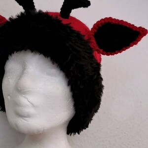 Puede incluir: Un tocado caprichoso, hecho a mano, con una combinaci&oacute;n de colores rojo y negro. El sombrero tiene un ribete de piel sint&eacute;tica negra, cuernos negros y orejas negras con ribete rojo. El tocado se muestra en una cabeza de maniqu&iacute; blanca.