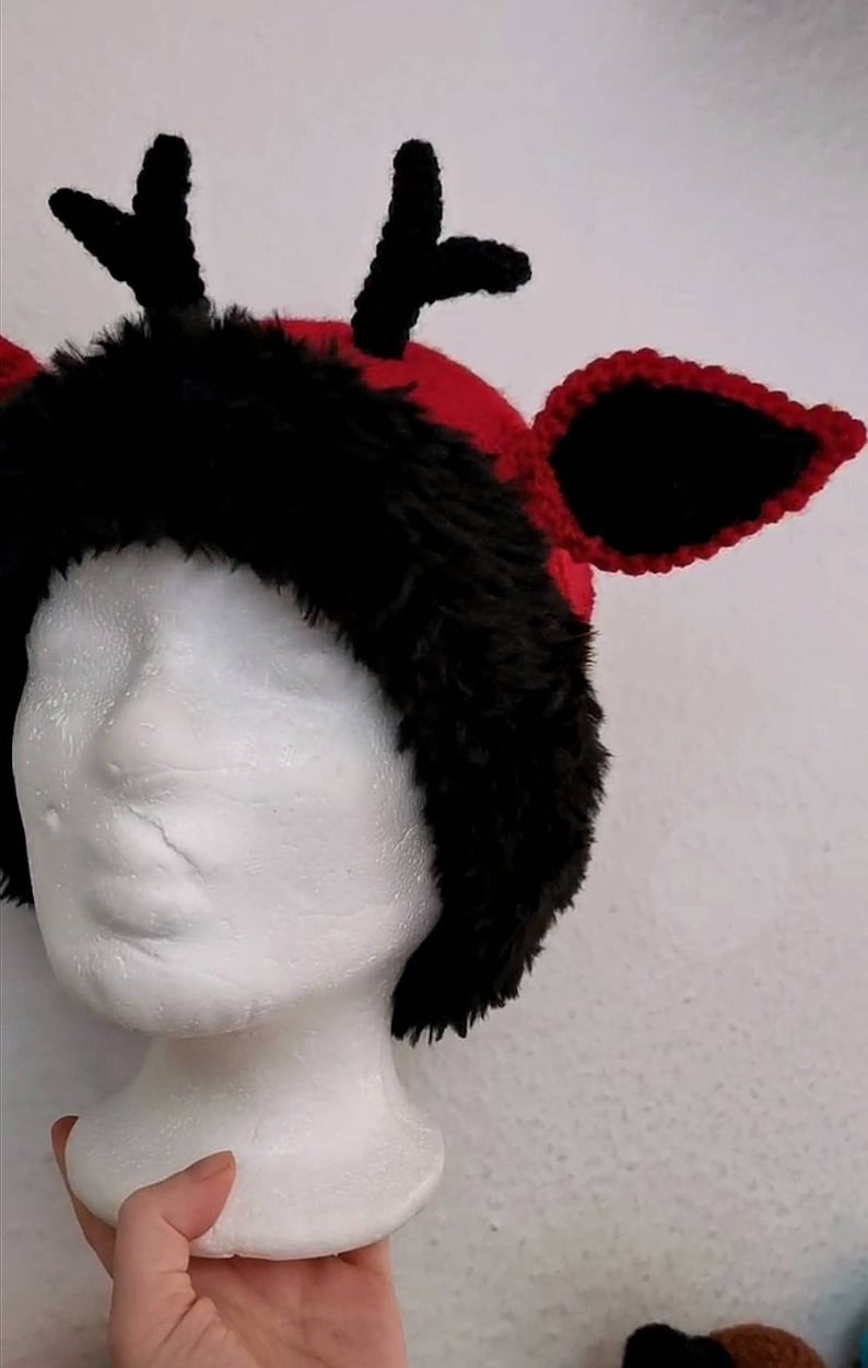 Puede incluir: Un tocado caprichoso, hecho a mano, con una combinaci&oacute;n de colores rojo y negro. El sombrero tiene un ribete de piel sint&eacute;tica negra, cuernos negros y orejas negras con ribete rojo. El tocado se muestra en una cabeza de maniqu&iacute; blanca.